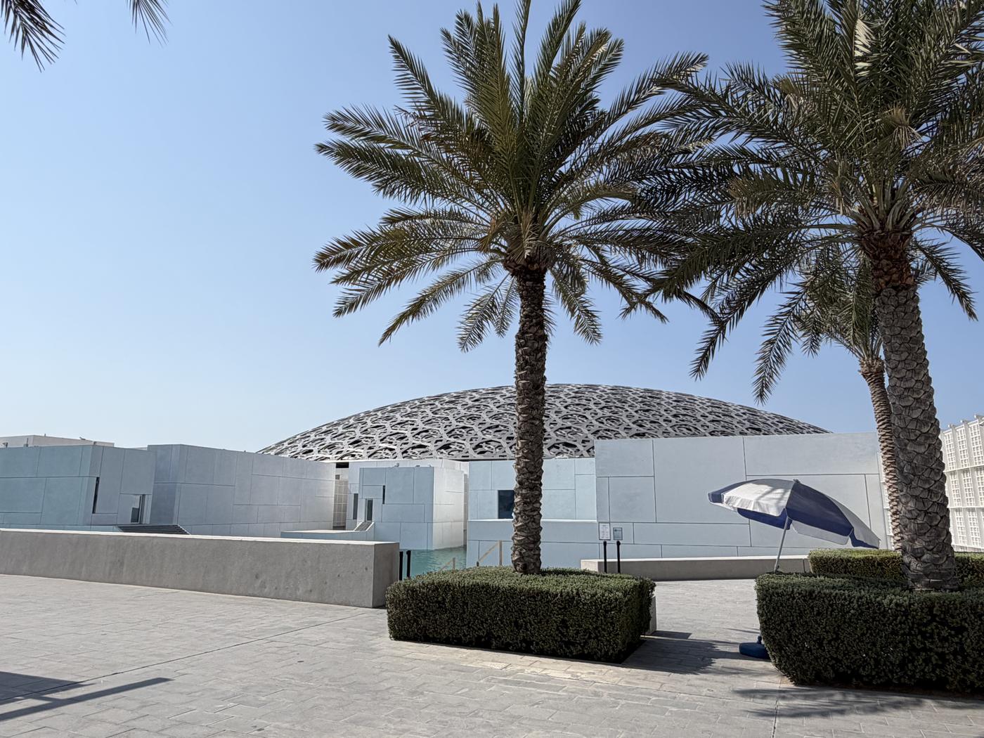 Die Kuppel des Louvre Abu Dhabi hinter Palmen